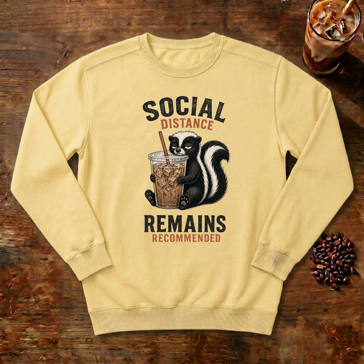 Social Distance Remains Skunk Sweatshirt in Butter, a retro skunk sipping iced coffee
