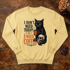 I Don't Need Therapy Cat Sweatshirt in Butter, a black cat holding a coffee mug and sitting on a skull