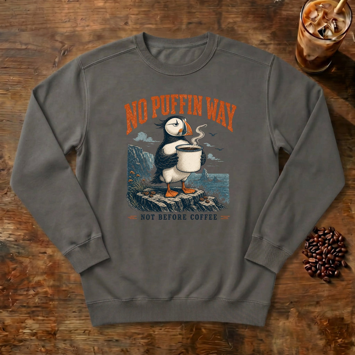 No Puffin Way Sweatshirt in Pepper, a puffin holding a cup of coffee by the coast