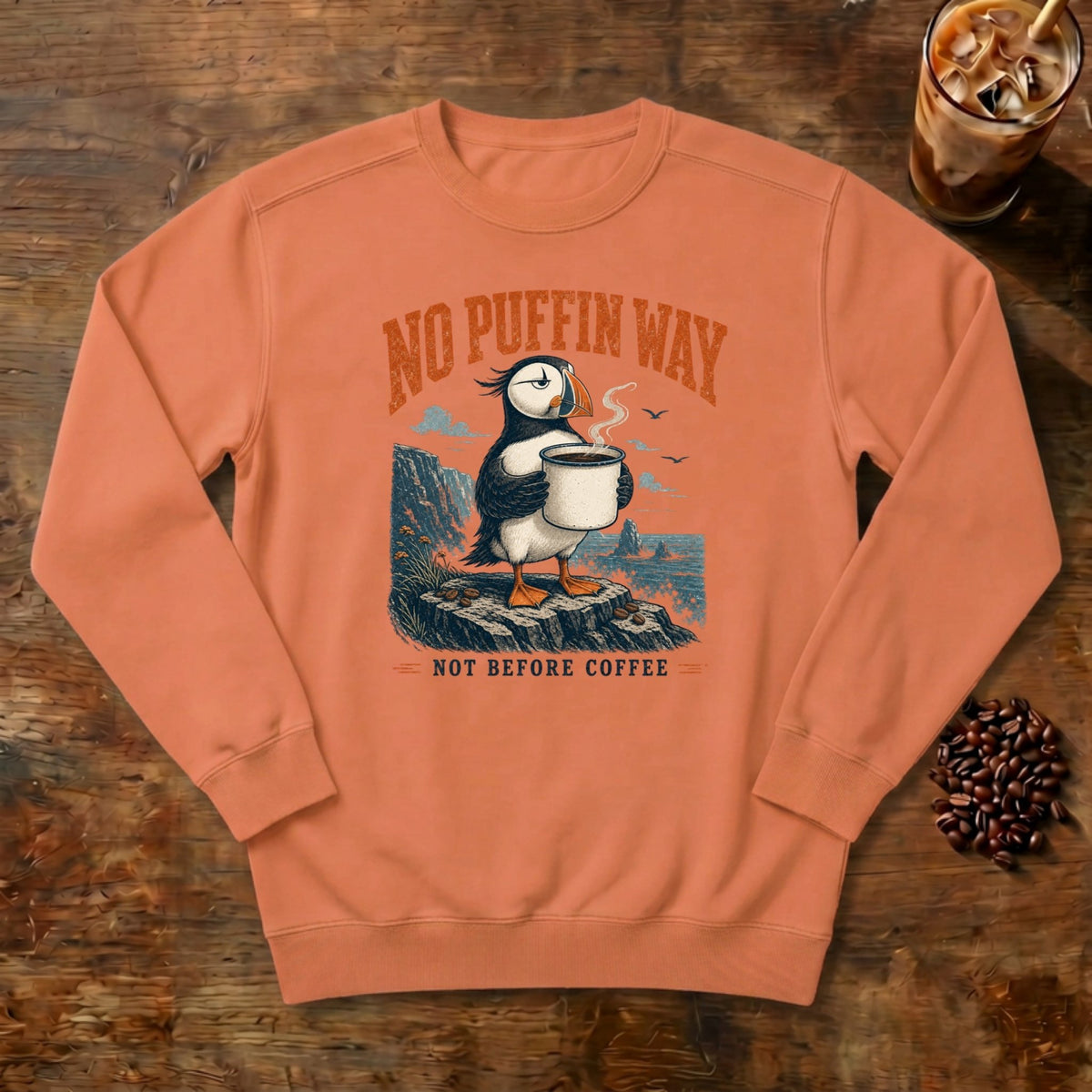 No Puffin Way Sweatshirt in Terracotta, a puffin holding a cup of coffee by the coast