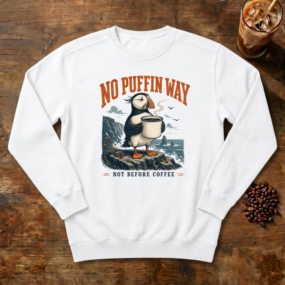 No Puffin Way Sweatshirt in White, a puffin holding a cup of coffee by the coast