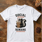 Skunk holding an iced coffee beneath the words Social Distance Remains Recommended on a White T-shirt.