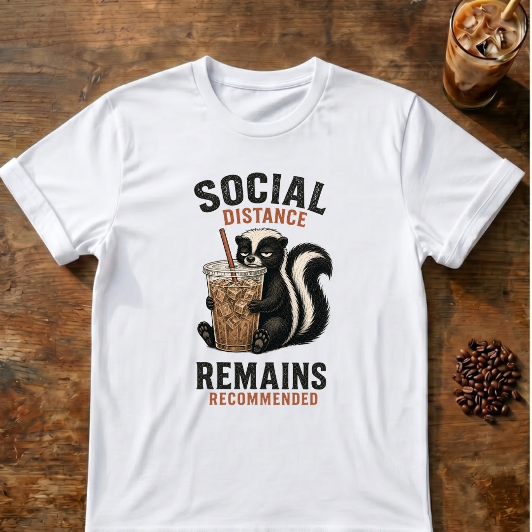 Skunk holding an iced coffee beneath the words Social Distance Remains Recommended on a White T-shirt.