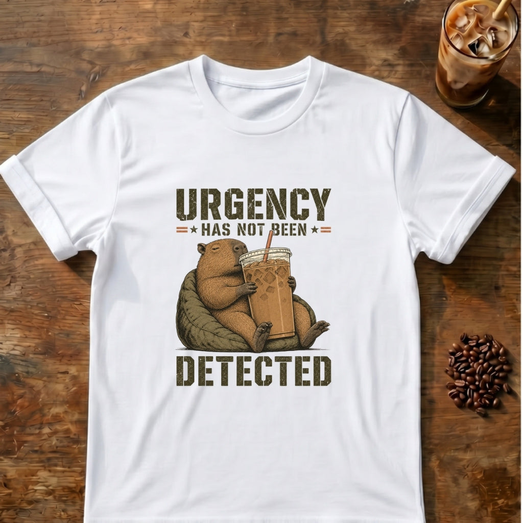Relaxed capybara holding a giant iced coffee beneath the words Urgency Has Not Been Detected on a White T-shirt.