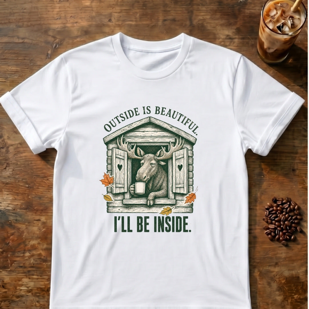 Content moose leaning out of a rustic cabin window holding a mug among autumn leaves with the words Outside Is Beautiful. I'll Be Inside on a White T-shirt.