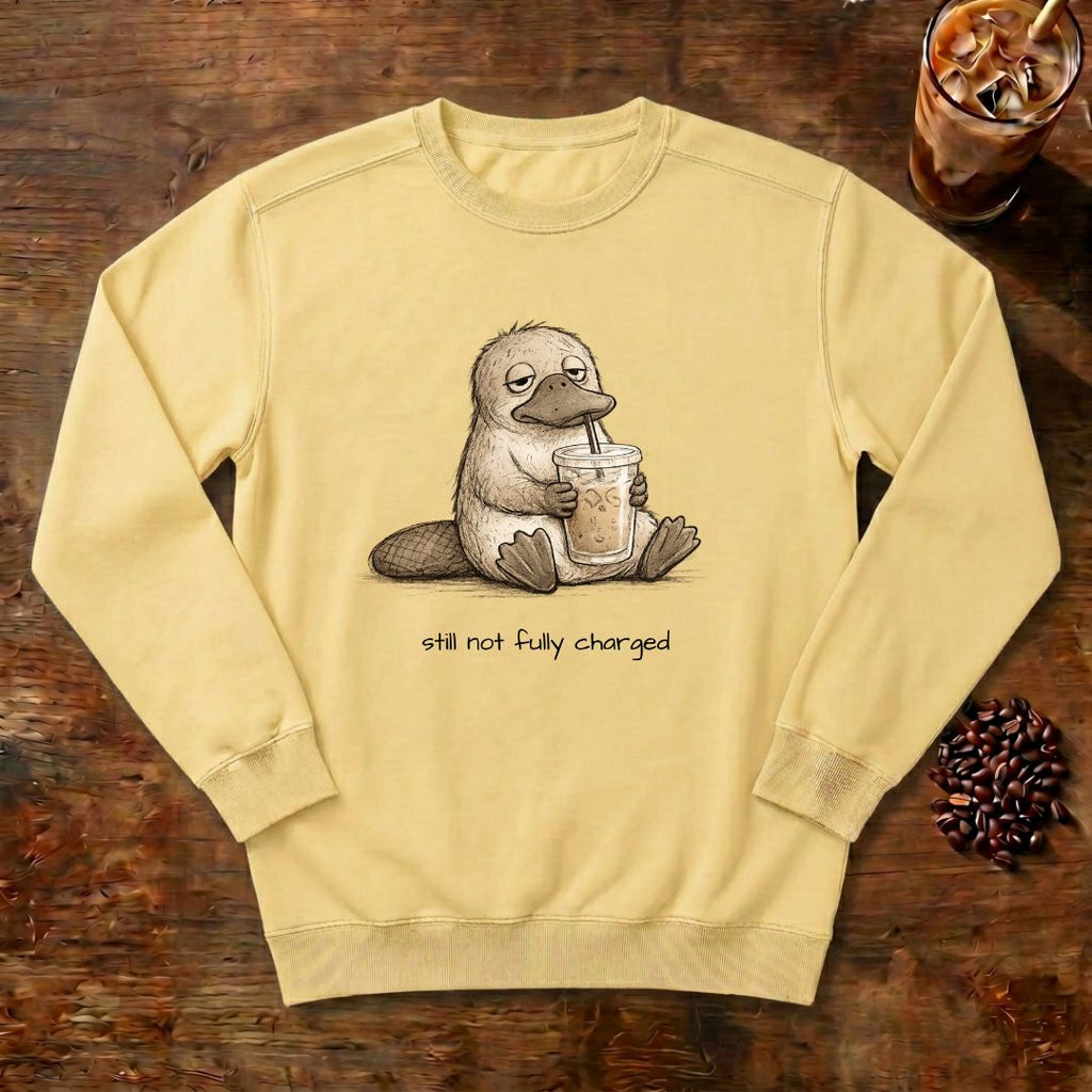 Still Not Fully Charged Platypus Sweatshirt in Butter, a sleepy platypus sipping iced coffee