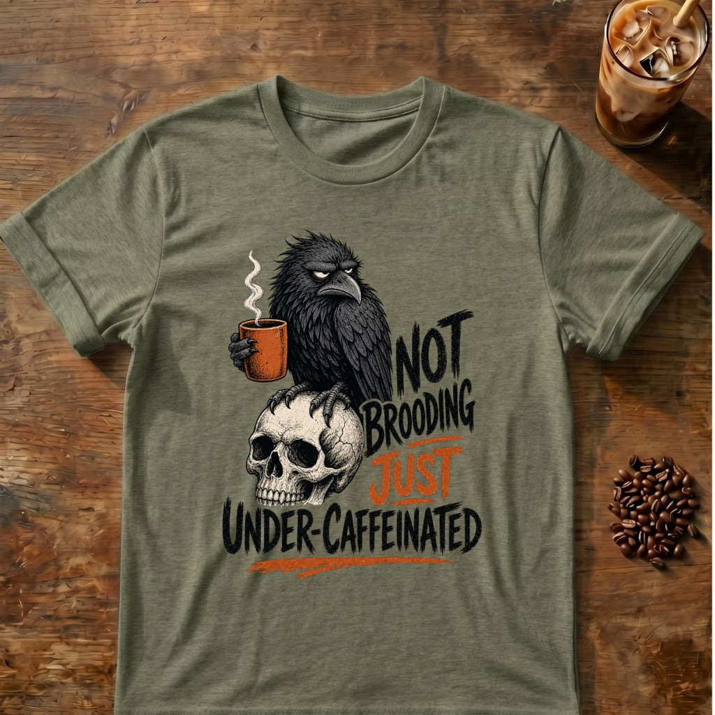 Irritated raven holding an orange coffee mug while perched on a skull with the words Not Brooding, Just Under-Caffeinated.