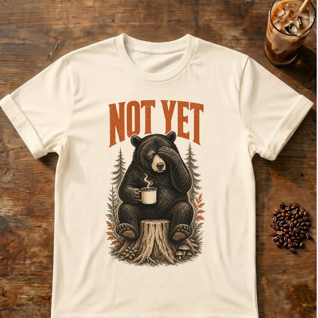 Exhausted black bear sitting on a tree stump with coffee and covering its face beneath distressed orange “Not Yet” text