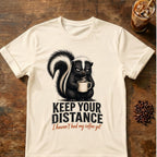 Grumpy skunk holding a steaming coffee mug above distressed text reading Keep Your Distance, with orange script saying I haven’t had my coffee yet. Natural