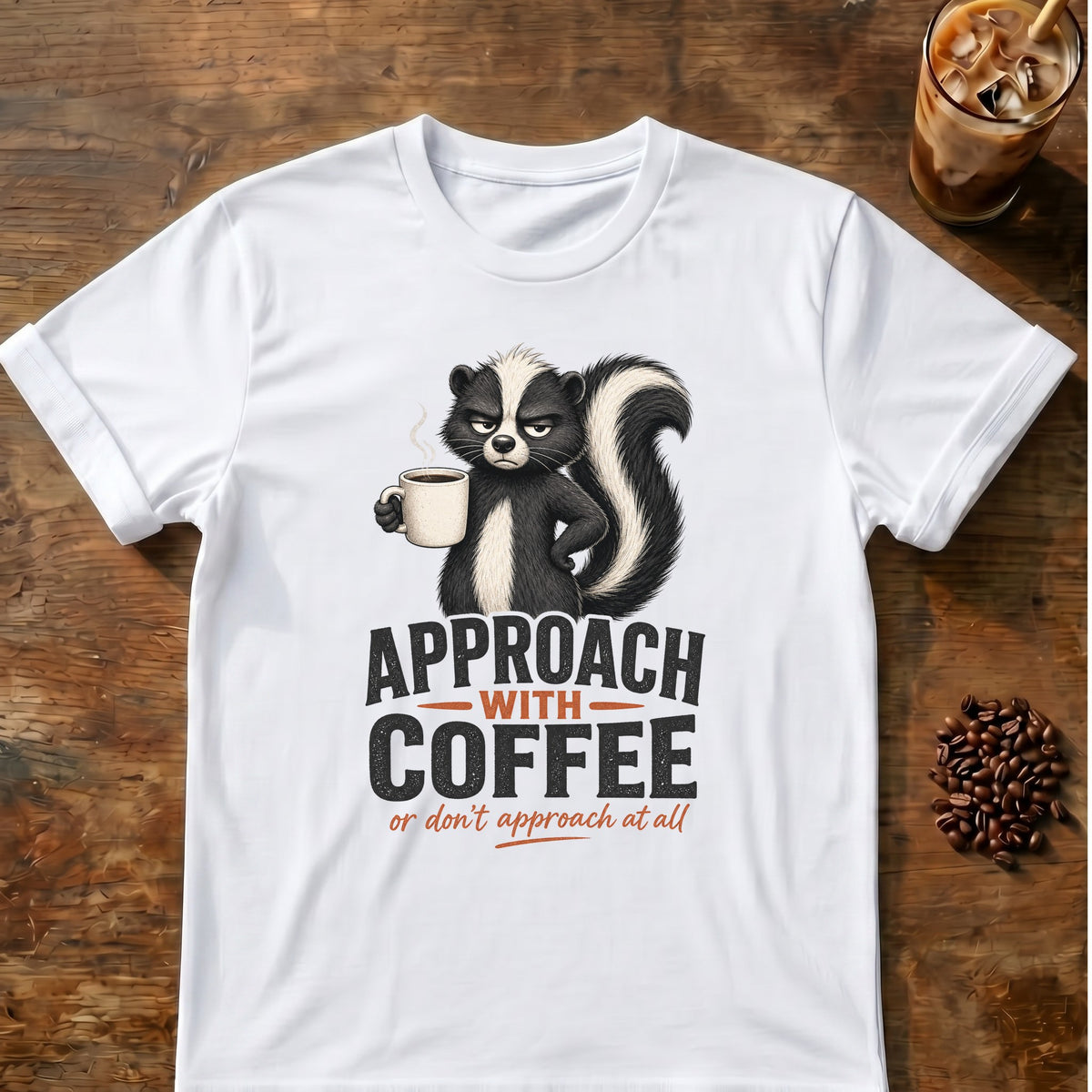 Grumpy skunk holding a steaming coffee mug above bold text reading Approach With Coffee, with orange script below saying or don’t approach at all. White